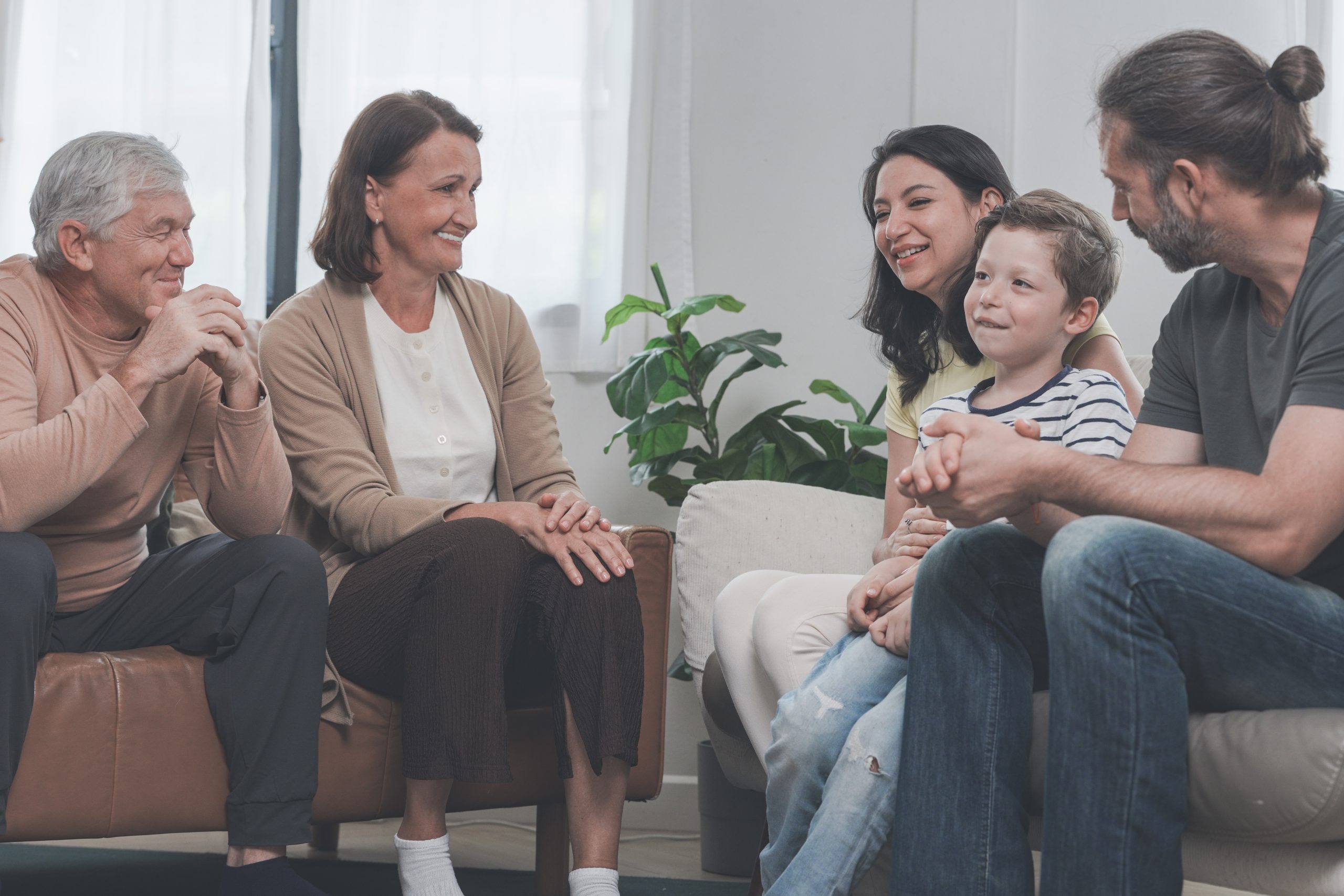 Three generations of one family hug and play on the living-room sofa in a warm, sunlit lounge, making everyday memories together, enjoying a relaxed day of togetherness at home.